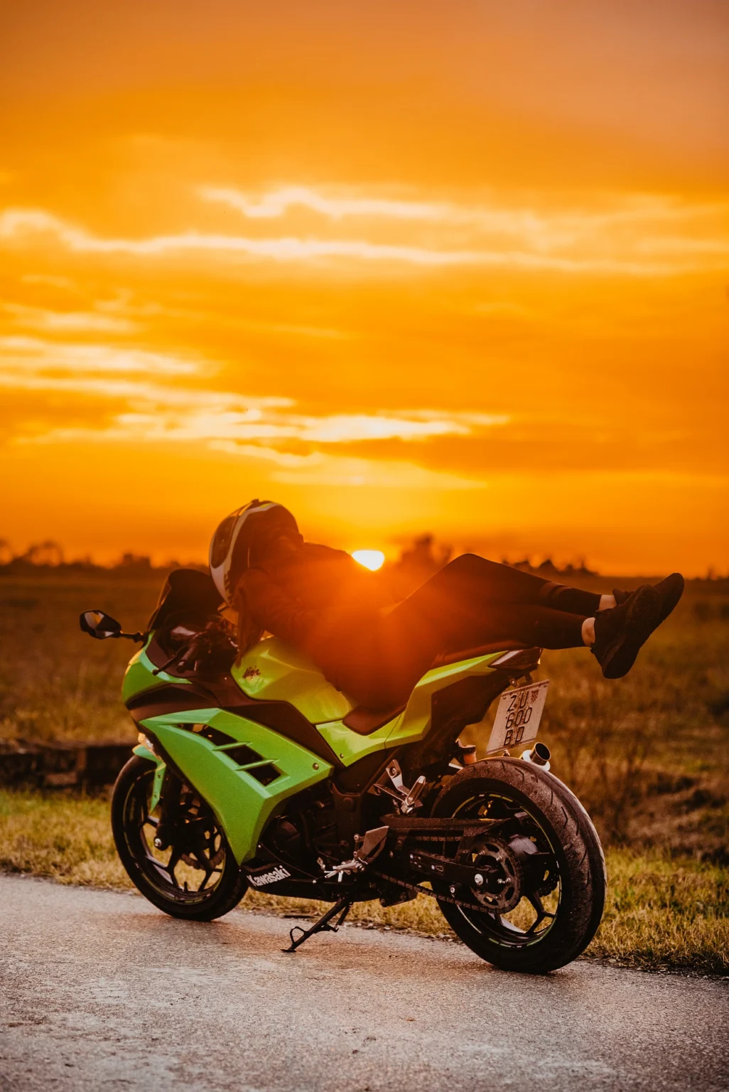 Female biker laying down on her green Kawasaki Ninja motorcycle on a road in Vienna. The image showcases her stylish pose and the sleek design of the bike against an urban backdrop