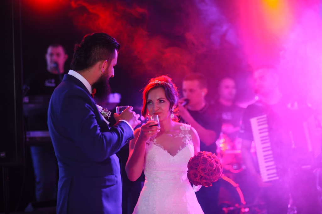 Bride and groom dancing under a chandelier-lit ballroom, surrounded by elegantly dressed guests raising their glasses in a joyful celebration.Would you like a version with more focus on candid or editorial reception moments?