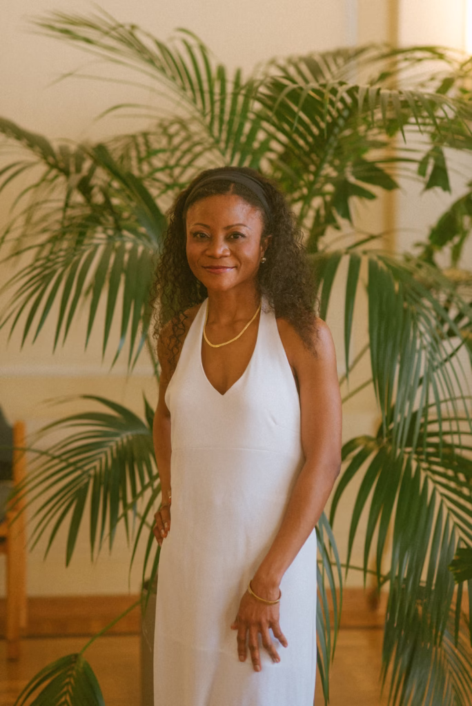 A Black bride standing elegantly in front of a lush green wall, her gown flowing beautifully, exuding confidence and timeless sophistication in a luxury wedding portrait.