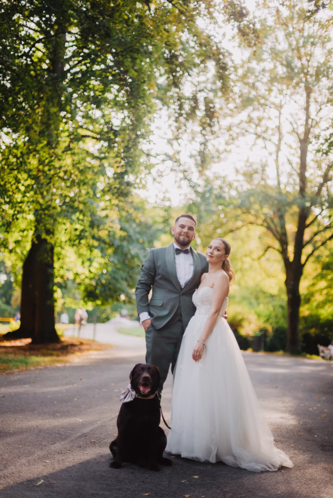 A bride and groom elegantly posing with their dog in a luxury wedding setting, the couple’s refined attire contrasting beautifully with their furry companion’s playful charm.